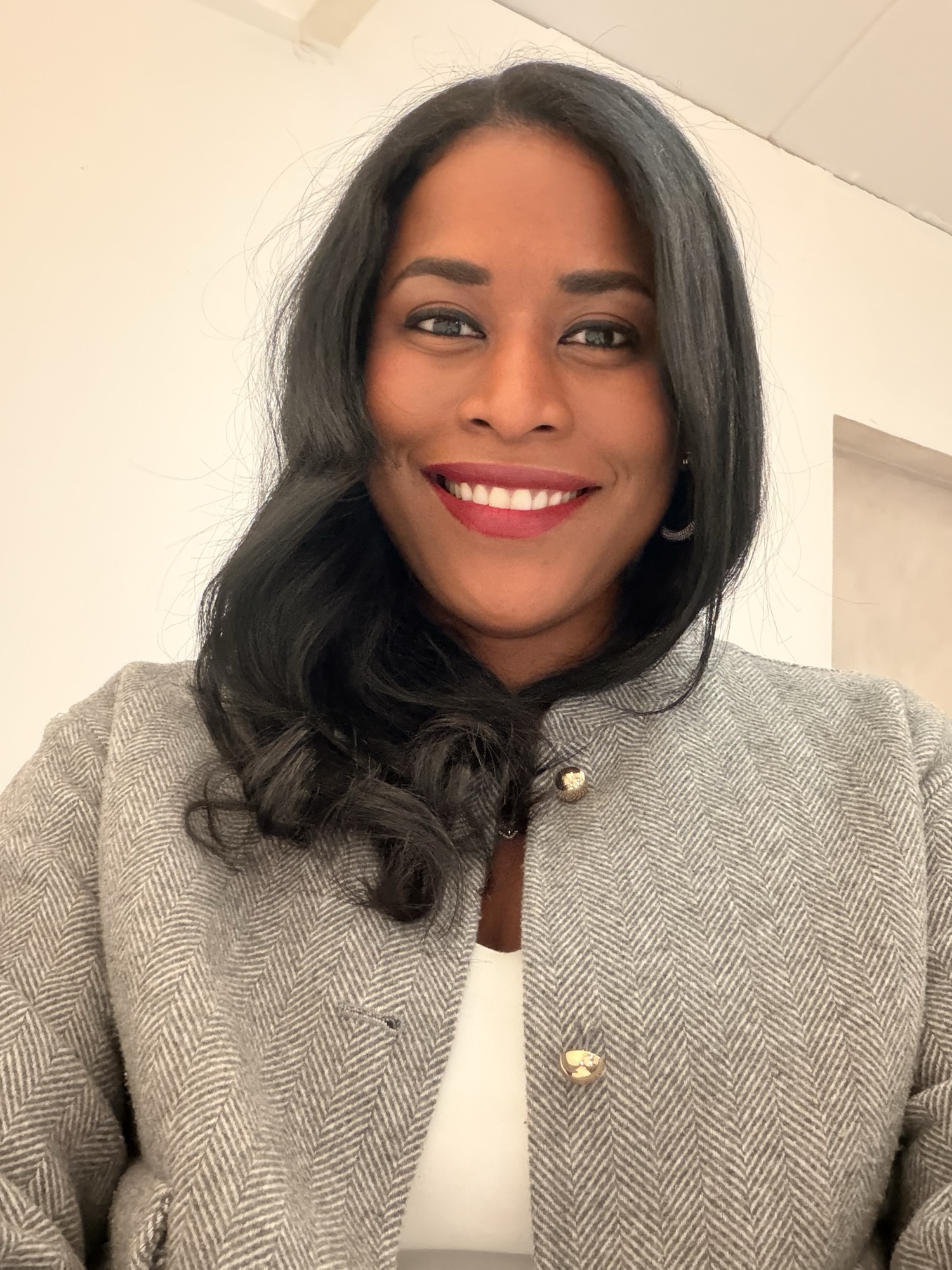 Smiling commercial headshot of Yazuri Guido in a grey herringbone jacket with gold buttons