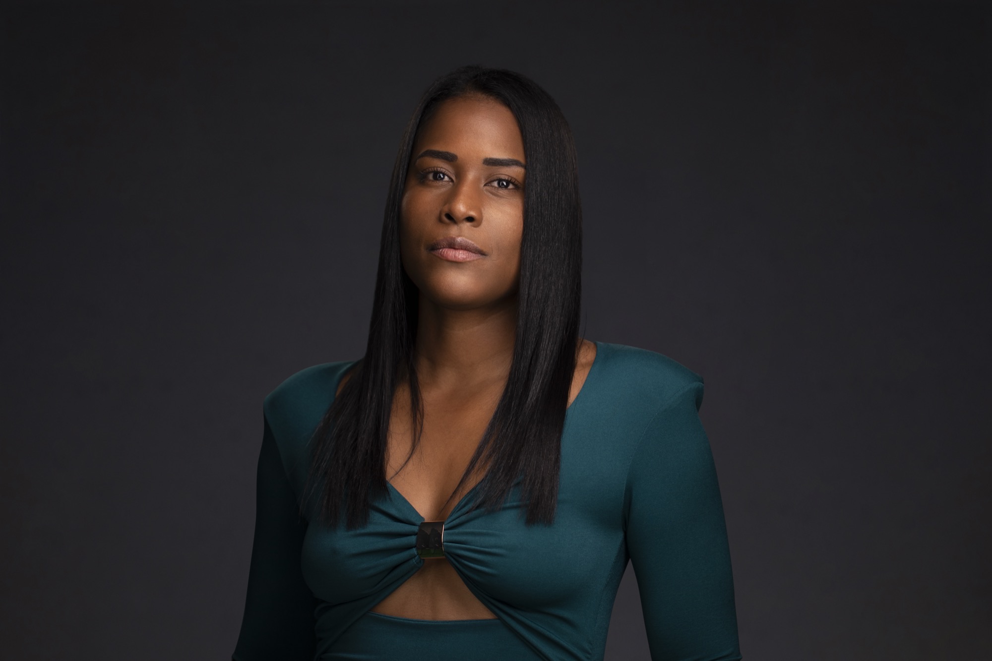 Studio headshot of Yazuri Guido in a dark teal dress with gold clasp detail against a charcoal background
